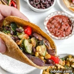 Vegan Roasted Veggie Tacos in a white plate with ingredients in the background against a white surface