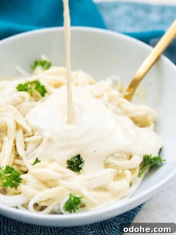 A bowl of pasta with Alfredo sauce being poured on it.