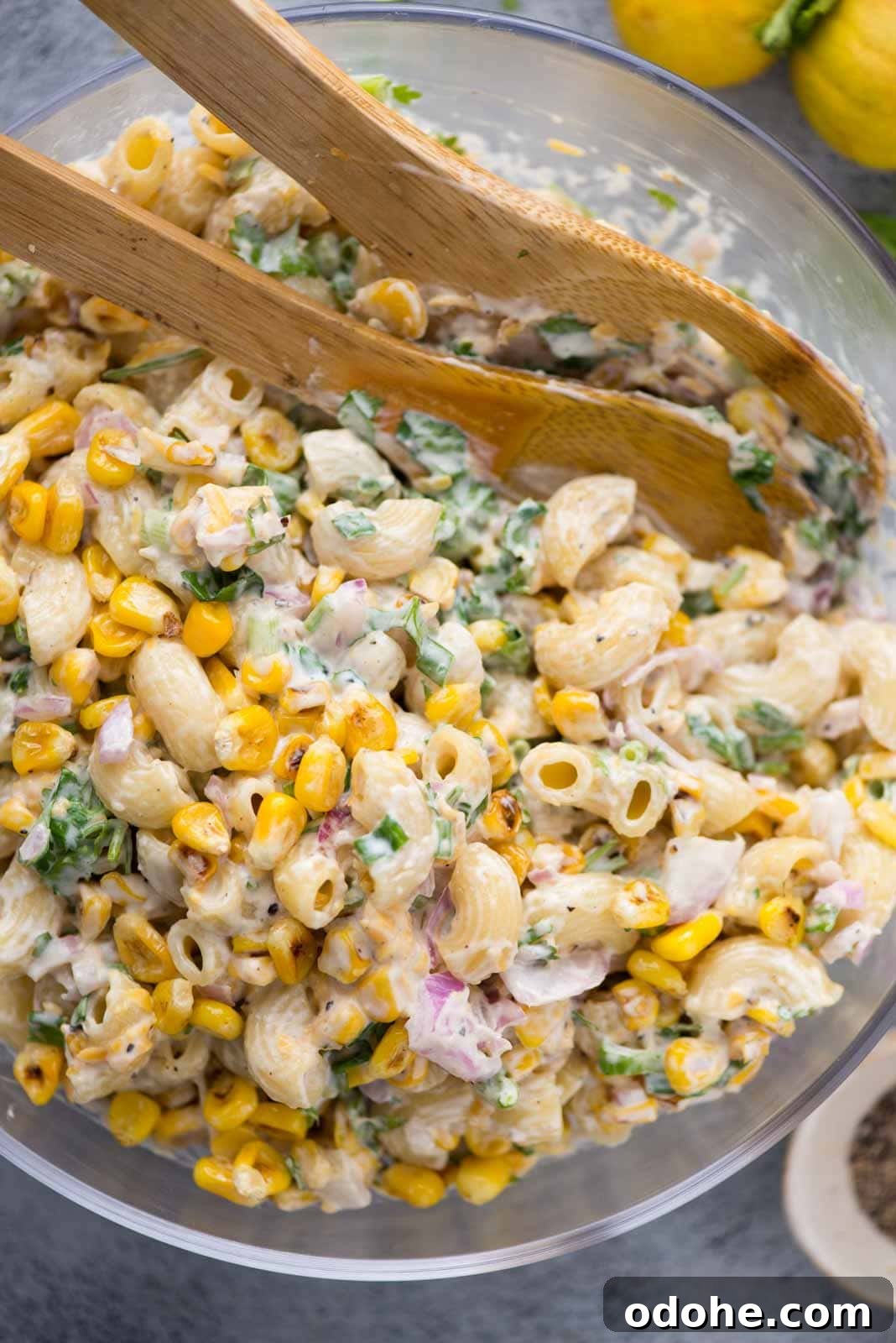 Corn pasta salad with mayo dressing Roasted corn pasta salad tossed in a mayo-based dressing with wooden spatulas.