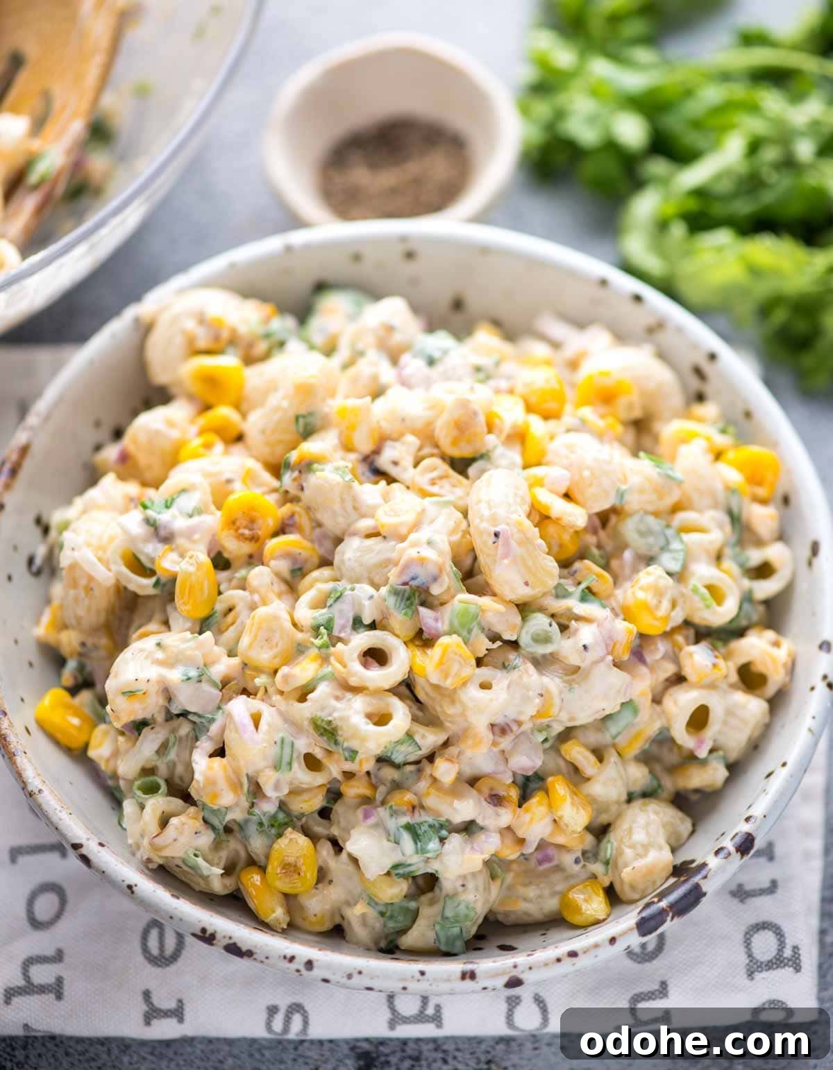 Corn Pasta Salad served in a bowl Corn pasta salad with green onions and coriander leaves mixed in mayo dressing served in a white spotted bowl.