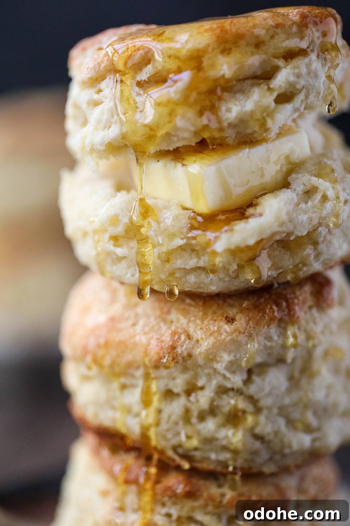 Southern buttermilk biscuits stacked on a plate with honey dripping over the top.