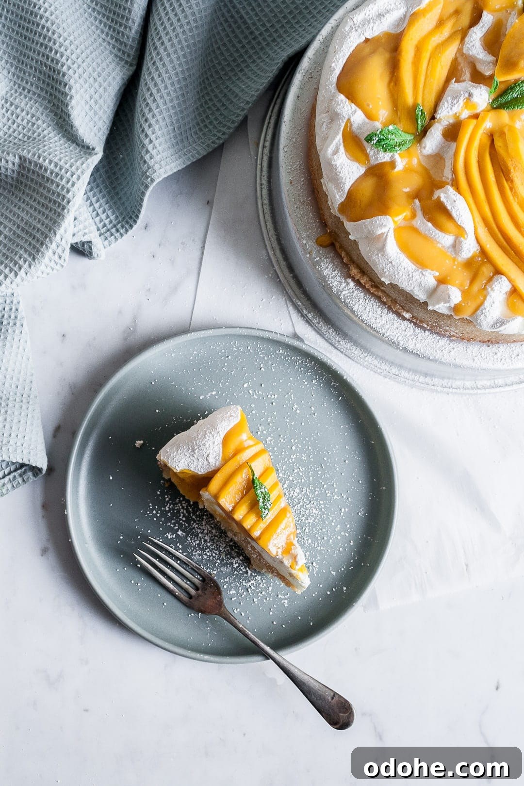 Slice of coconut meringue mango cake on a blue plate with rest of cake nearby