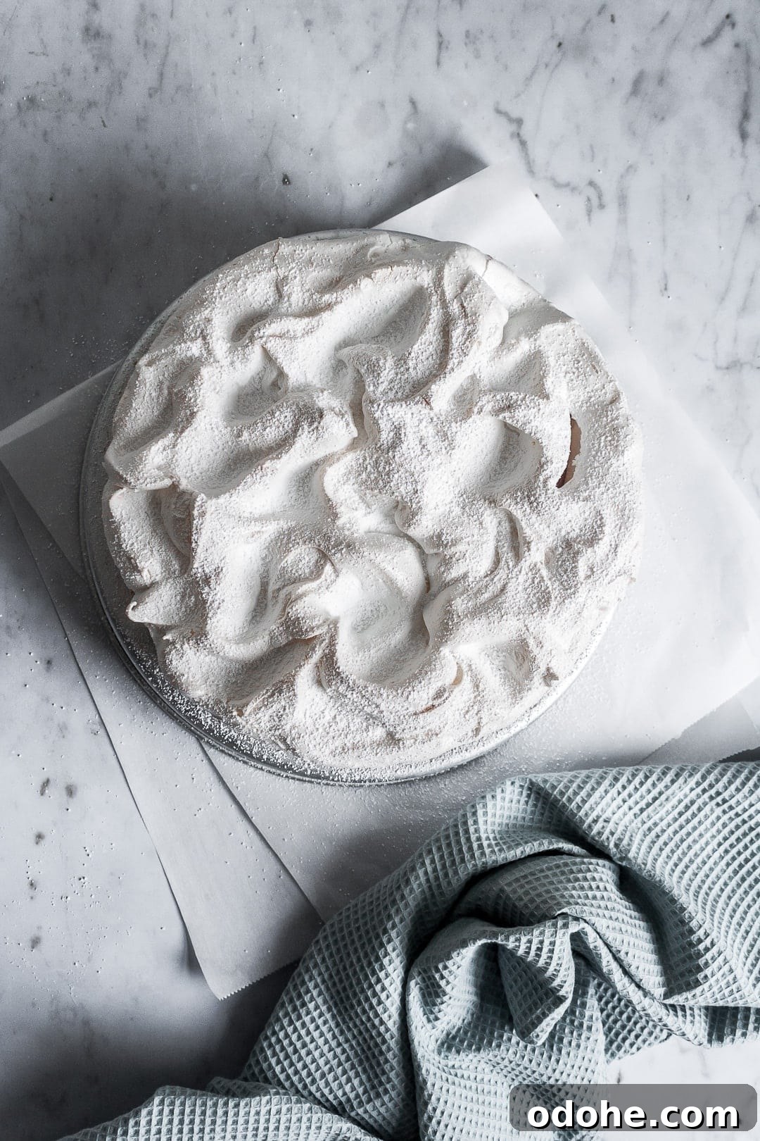 Top view of baked meringue covering a layer cake - on a marble background with parchment paper underneath