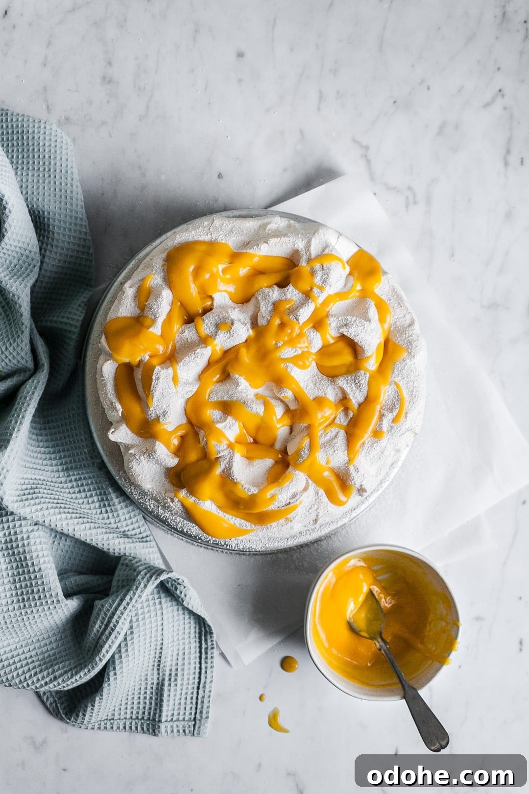 Meringue cake with mango sauce drizzled on top; small bowl of mango sauce next to cake