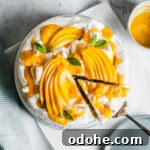 A coconut cake with baked meringue is decorated with vibrant yellow mango slices and mango puree. It rests on a white parchment square on a marble surface. A slice is being lifted out with a cake server.