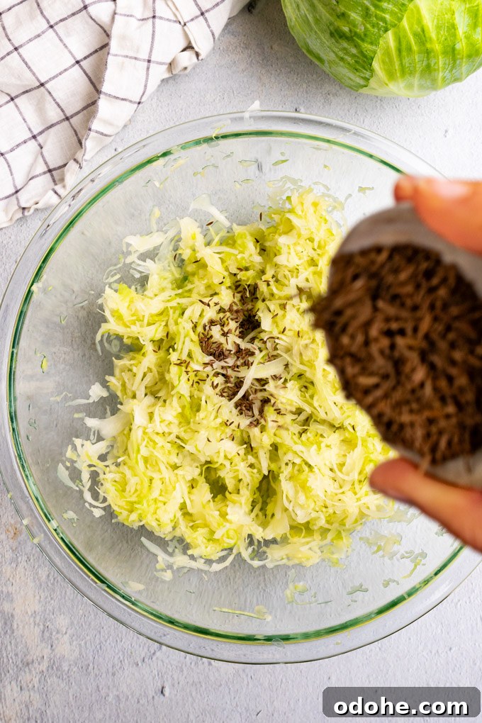 Caraway seeds are being added to a bowl of shredded cabbage that has been massaged, and prepared for sauerkraut.