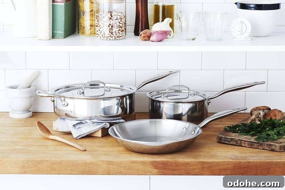 A set of stainless steel pots and pans from Heritage Steel sitting on a wooden countertop.