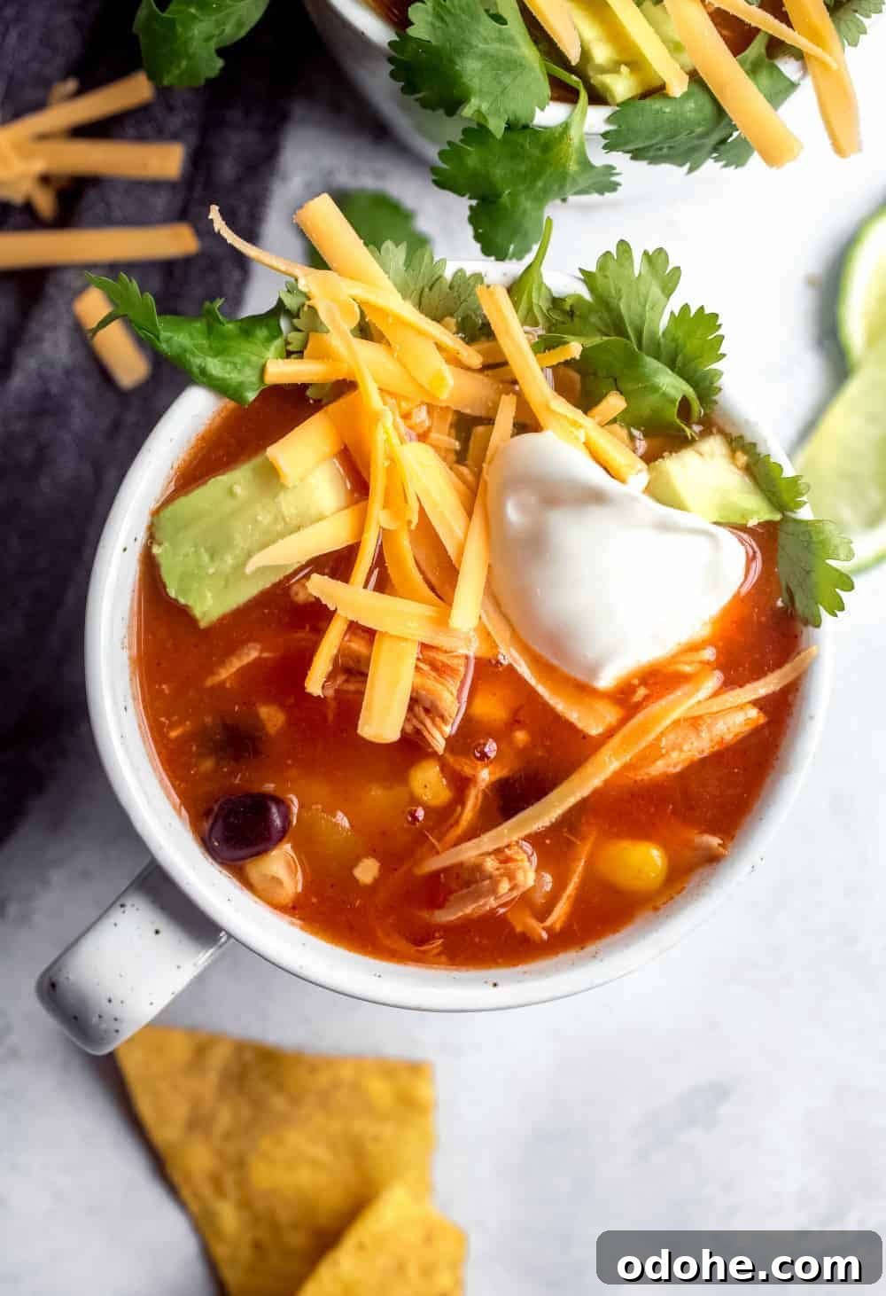Authentic Mexican Tortilla Soup Recipe with Crispy Tortilla Strips 6 Close up view of a mug of tortilla soup topped with cheese, sour cream and avocado