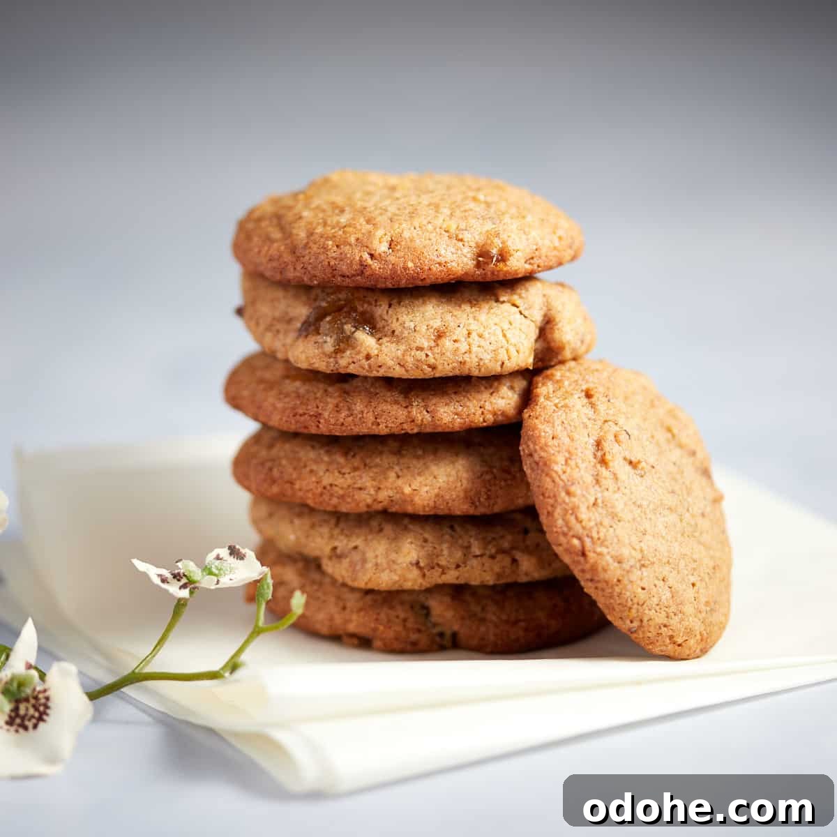 Photo of a stack of stem ginger cookies sitting on a white napkin with some flowers in front.