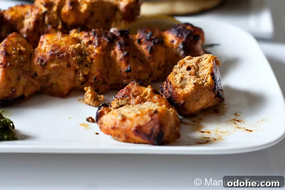 Chicken Tikka Close-up of cooked chicken tikka pieces on skewers served on a plate with light charring.