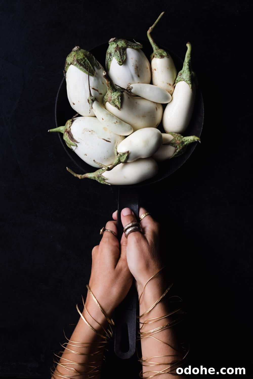 Cast iron skillet filled with white eggplant on a black background.