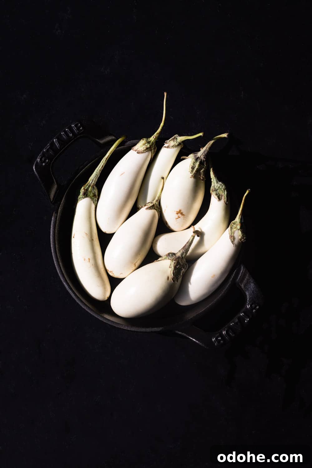 Overhead view of small white eggplants arranged in a black bowl on a dark background.
