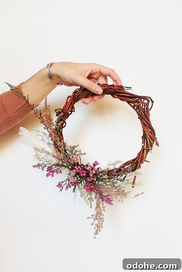Girl holding a DIY willow wreath with dried flowers on a white wall - tracking information
