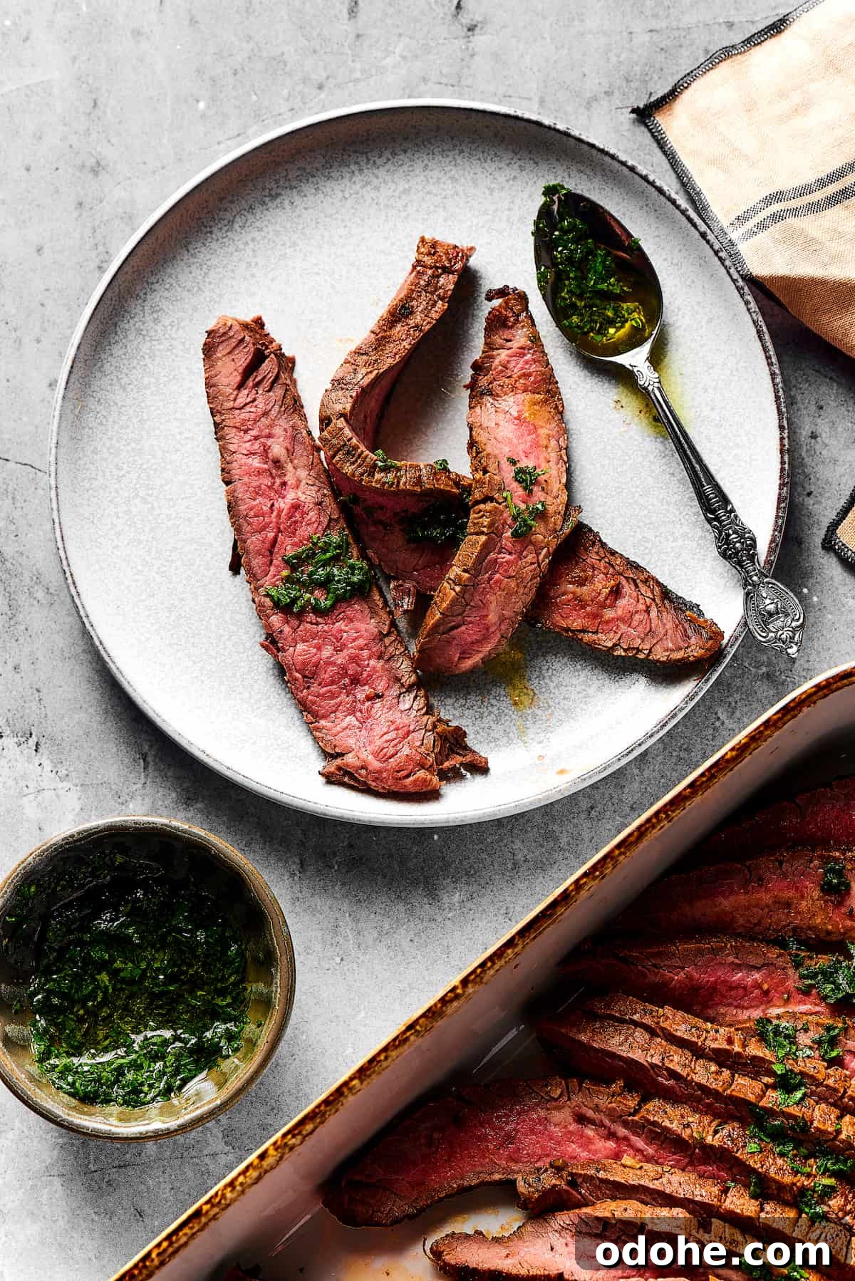 Orange and lime juice, garlic and jalapeno, maple and cumin - this easy Grilled Carne Asada is drenched in a medley of mouthwatering flavors! A small plate with three strips of medium-rare grilled carne asada on it. Nearby is a large platter of the steak slices, a cup of sauce, and a spoon.