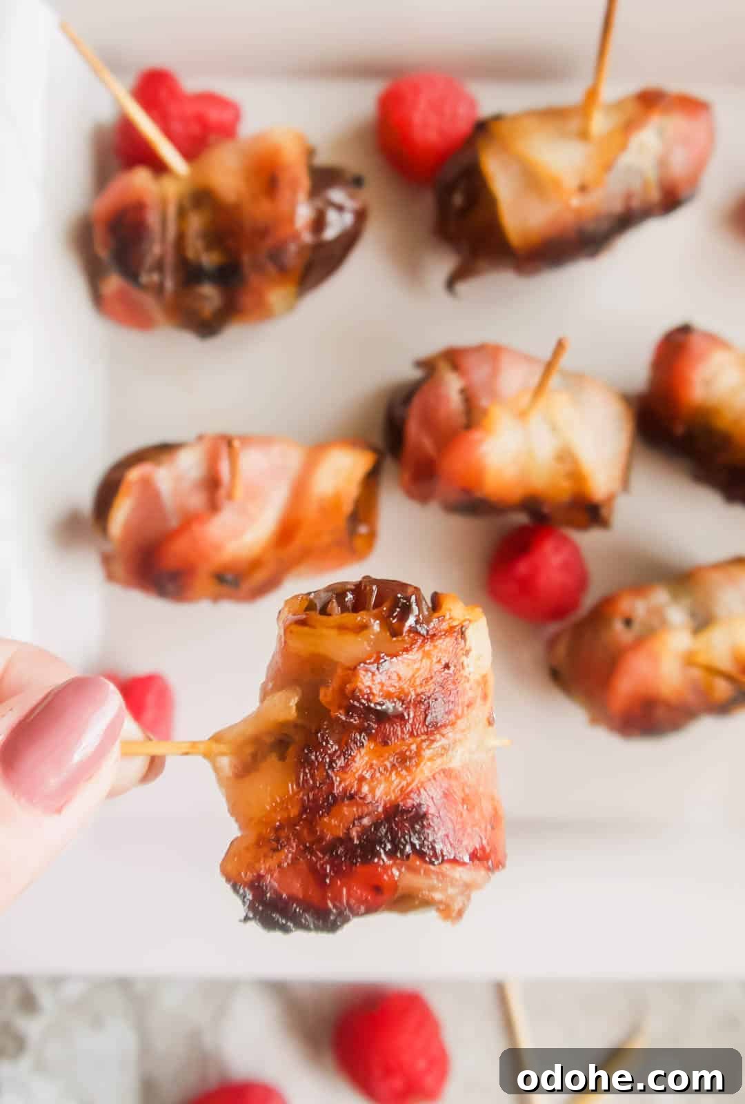 Bacon-Wrapped Raspberry-Stuffed Dates | Paleo & Whole30-Friendly 3 Raspberry stuffed medjool date covered in bacon being lifted by a tooth pick.