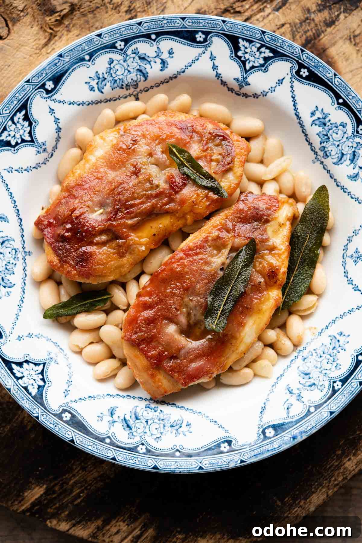 Chicken Saltimbocca Recipe: Tender Prosciutto-Wrapped Chicken with Sage 2 Two pieces of chicken saltimbocca on a plate on top of cannellini beans.