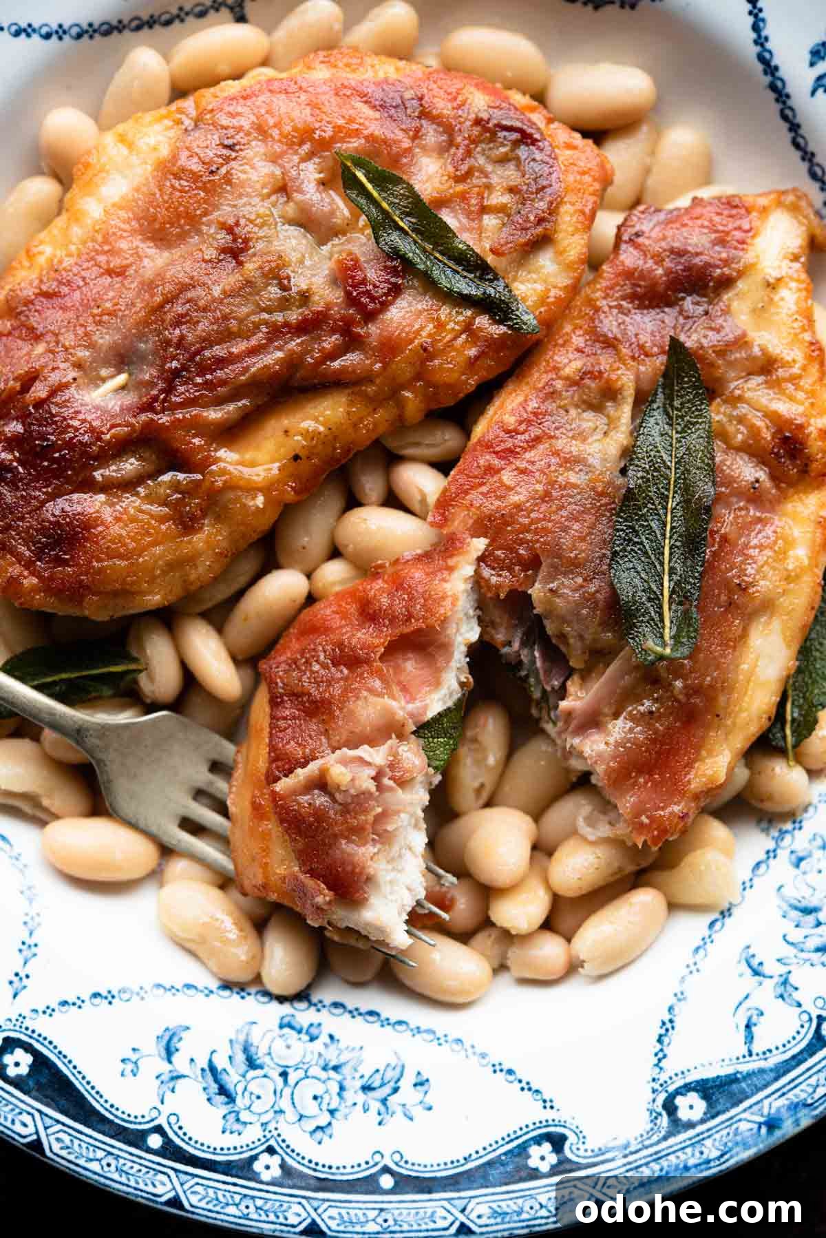 Chicken Saltimbocca Recipe: Tender Prosciutto-Wrapped Chicken with Sage 7 A close up of chicken saltimbocca on a plate with beans and sage.