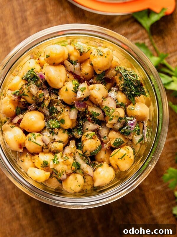 Marinated chickpeas in a mason jar with herbs, oil and seasoning sitting on a wooden board.