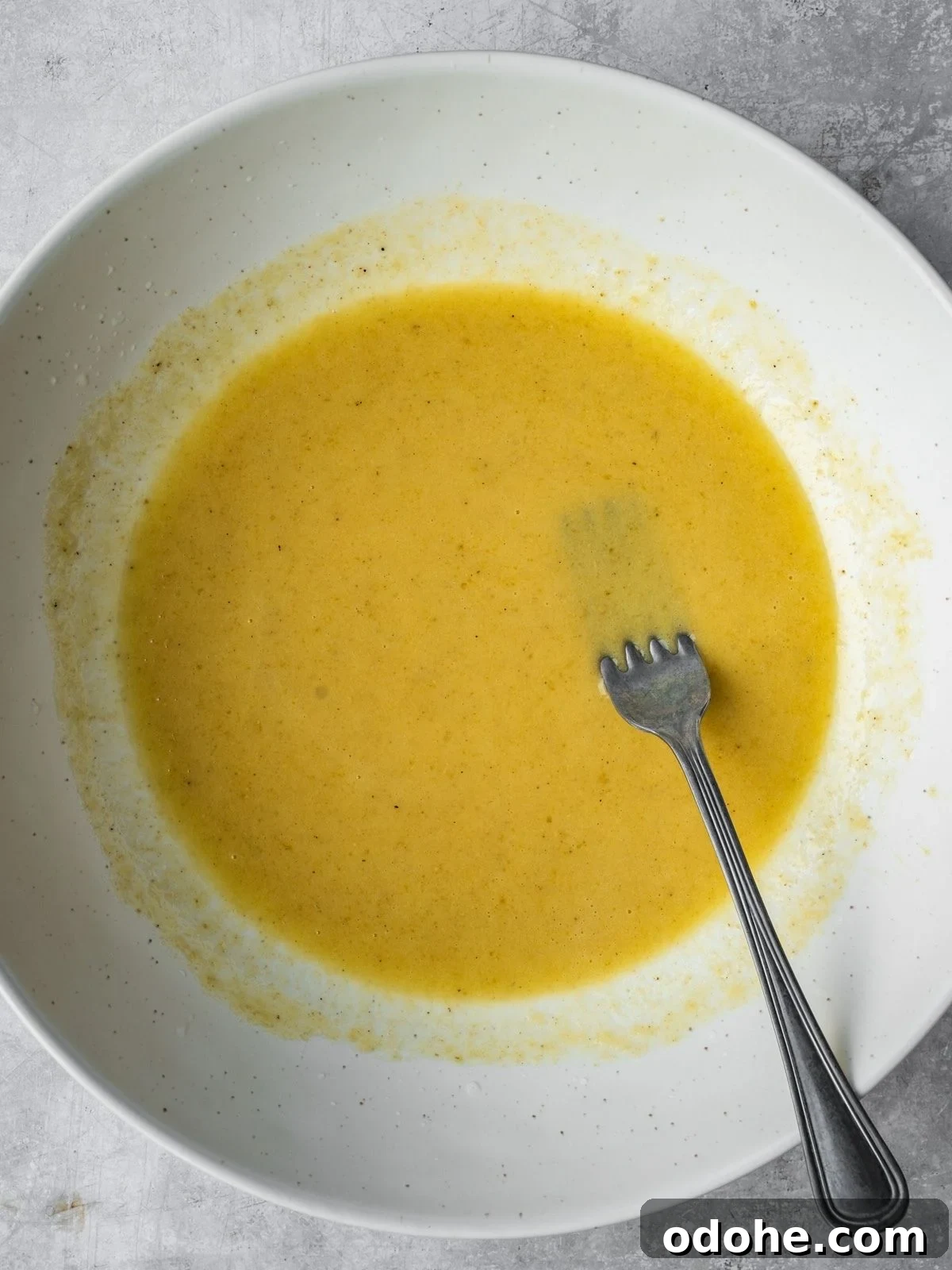 A bowl with mixed salad dressing ingredients including olive oil, tahini, honey, lemon juice, salt and pepper.
