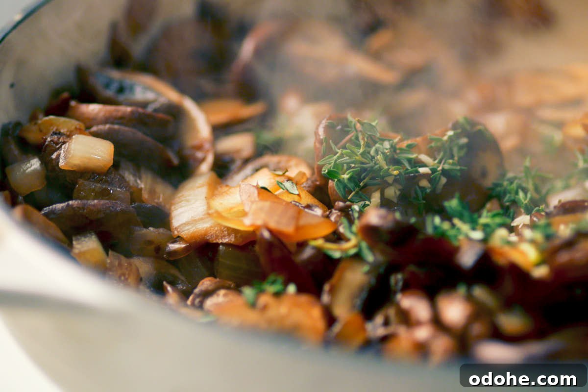 Adding garlic and thyme to sauteed mushrooms in a skillet for vegetarian strogranoff.