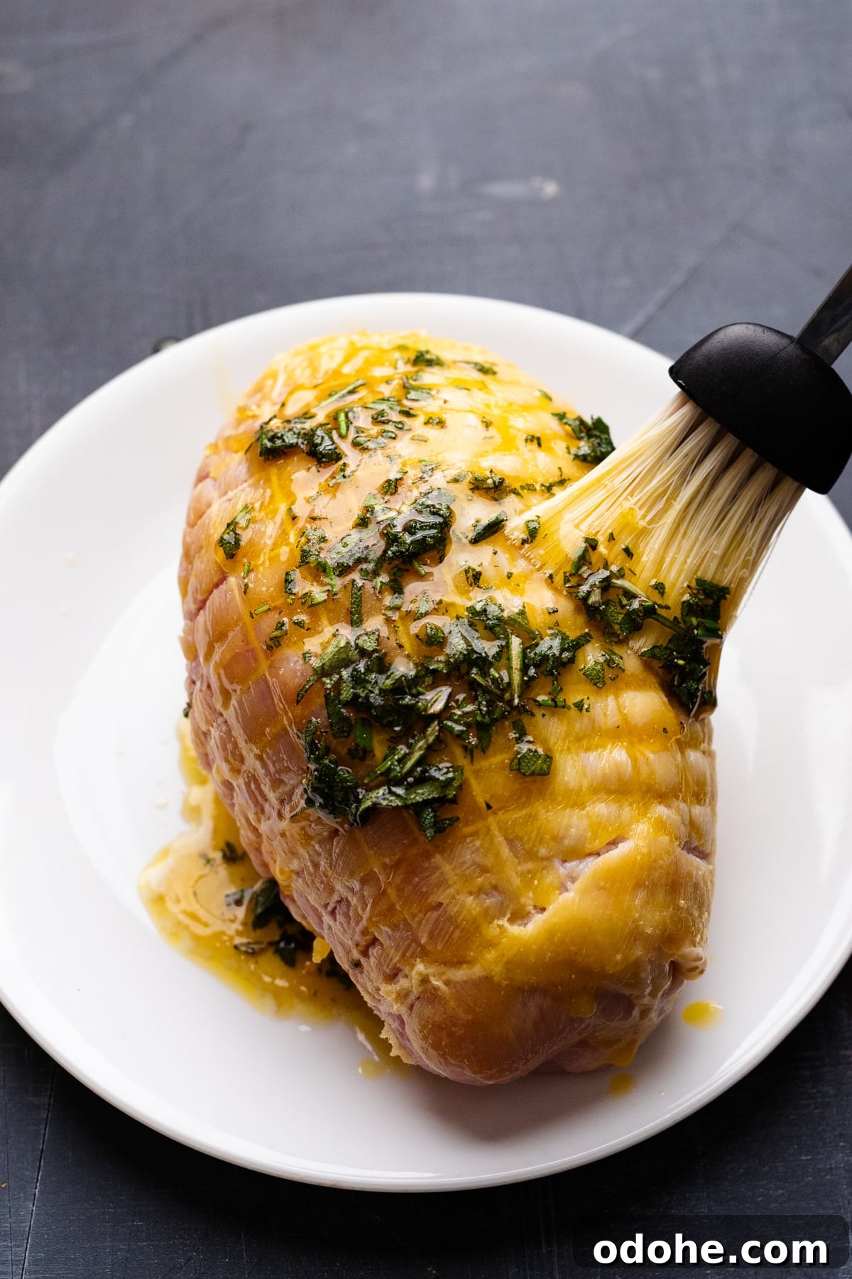 Maple Herb Turkey Breast in the Air Fryer: Juicy, Flavorful Roast 7 A brush basting herbs and butter on a turkey breast that's sitting on a white plate.