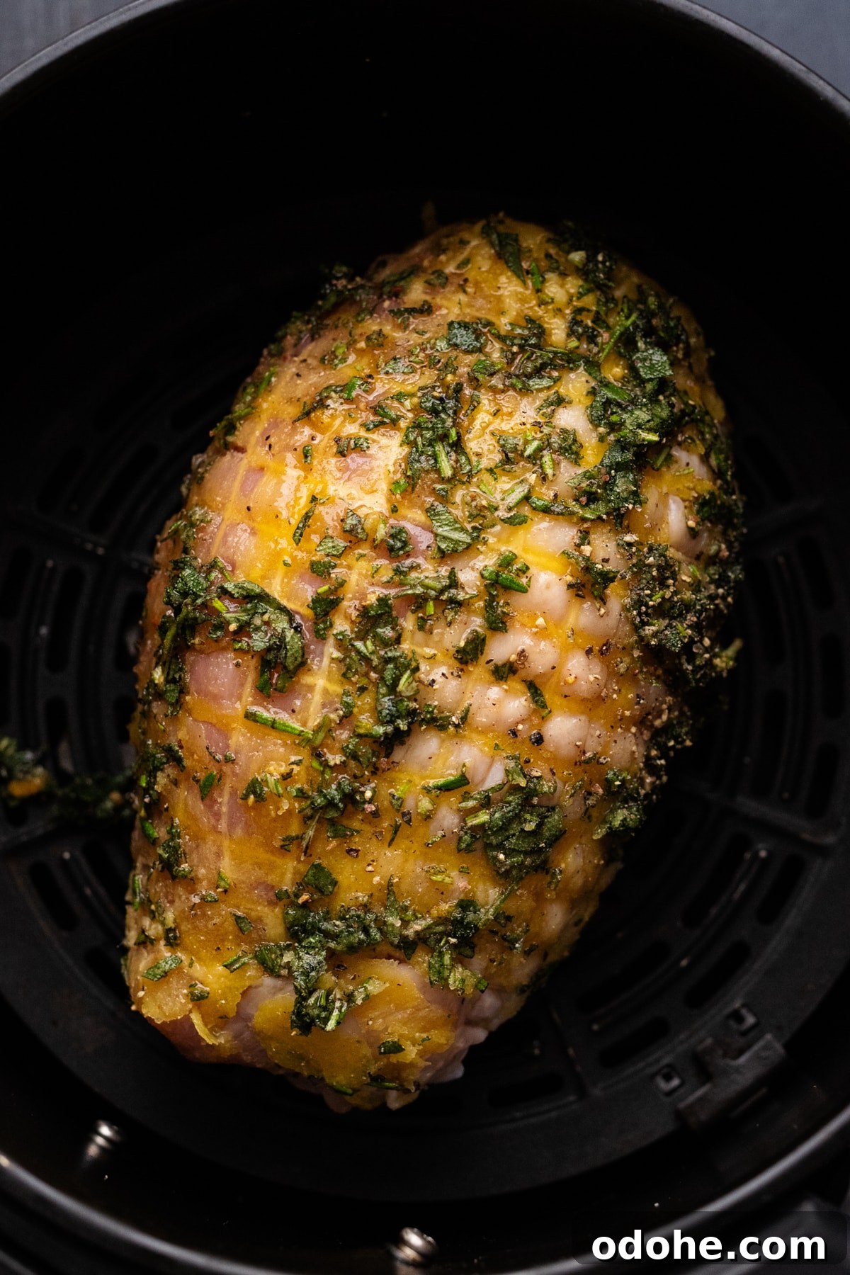 Maple Herb Turkey Breast in the Air Fryer: Juicy, Flavorful Roast 8 A turkey breast with chopped herbs on it in a black air fryer basket.