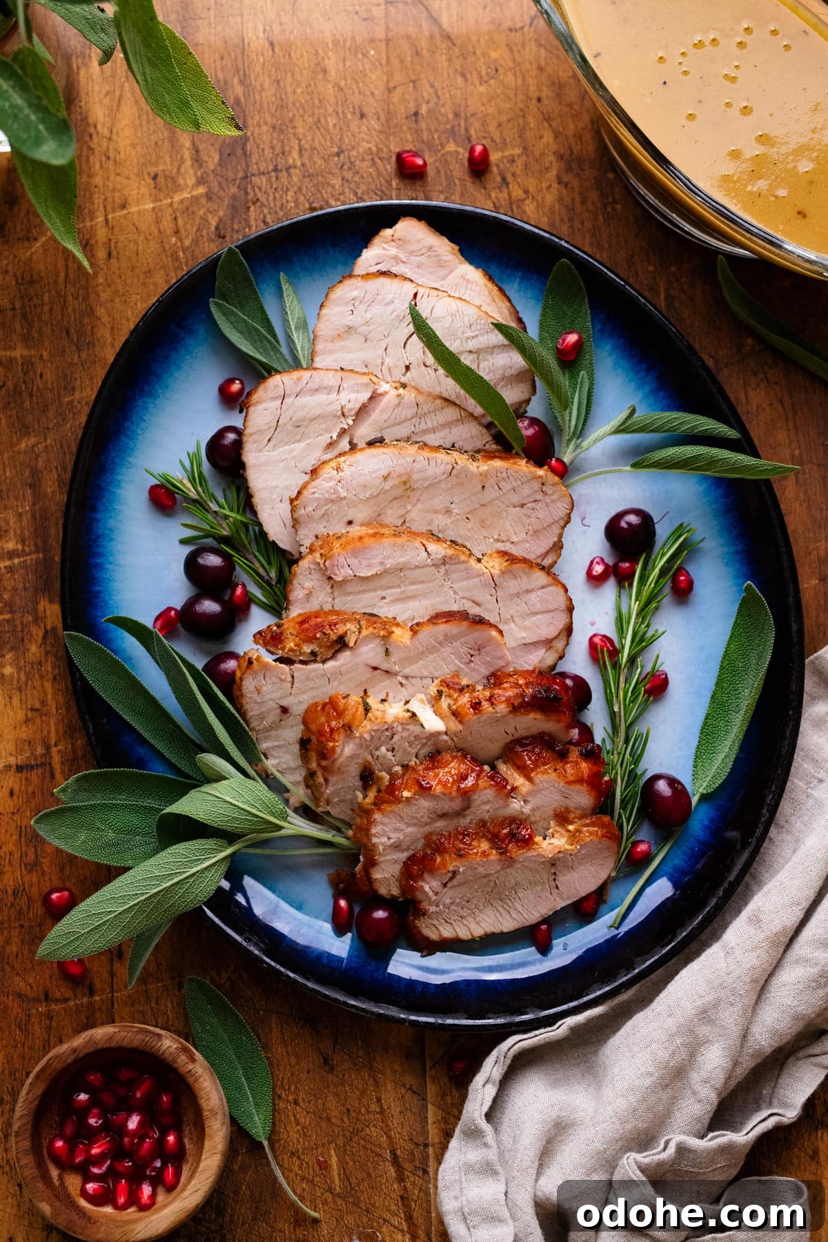 Maple Herb Turkey Breast in the Air Fryer: Juicy, Flavorful Roast 10 A blue plate with slices of air fryer turkey breast on it with fresh herbs arranged around it. The plate of turkey is arranged on a wooden background with herbs, gravy, and a gray napkin displayed around it.