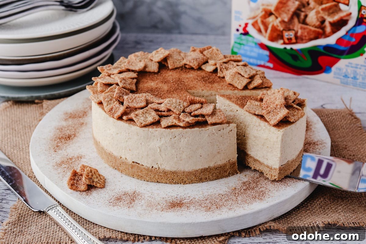 No-Bake Cheesecake Recipes: Simple, No-Oven Dessert Ideas 6 Serving a slice of Cinnamon Toast Crunch cheesecake from a serving board, with a pile of plates and box of Cinnamon Toast Crunch in the background.