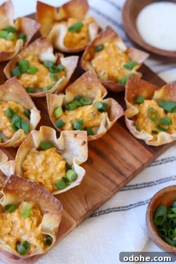 Wonton cups filled with buffalo chicken and green onion on platter.