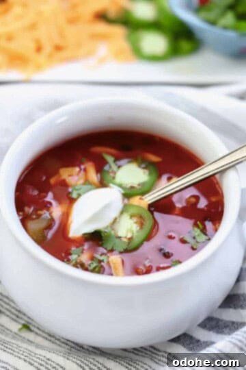 Dutch oven chili in bowl topped with sour cream, cheese and jalapeno