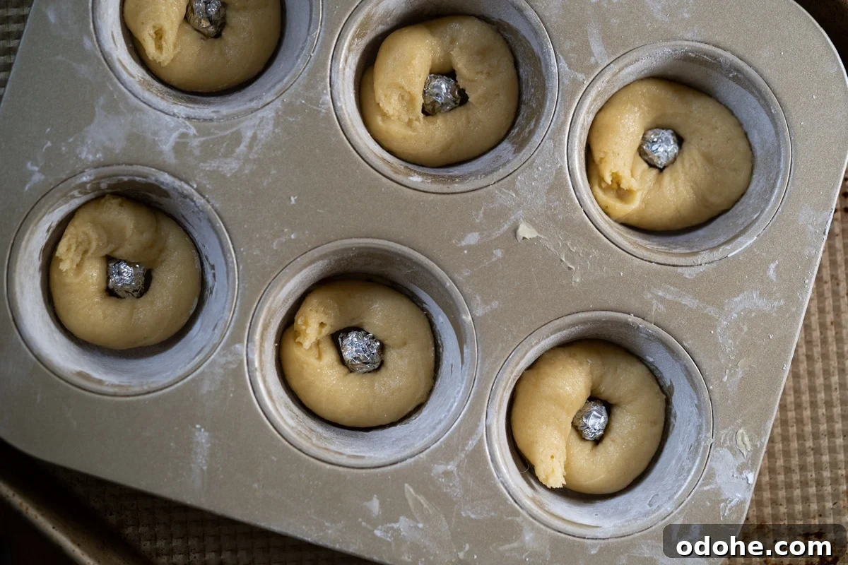 Showing how to make a makeshift donut pan by placing aluminum balls in the middle of muffin pan and piping the batter around it