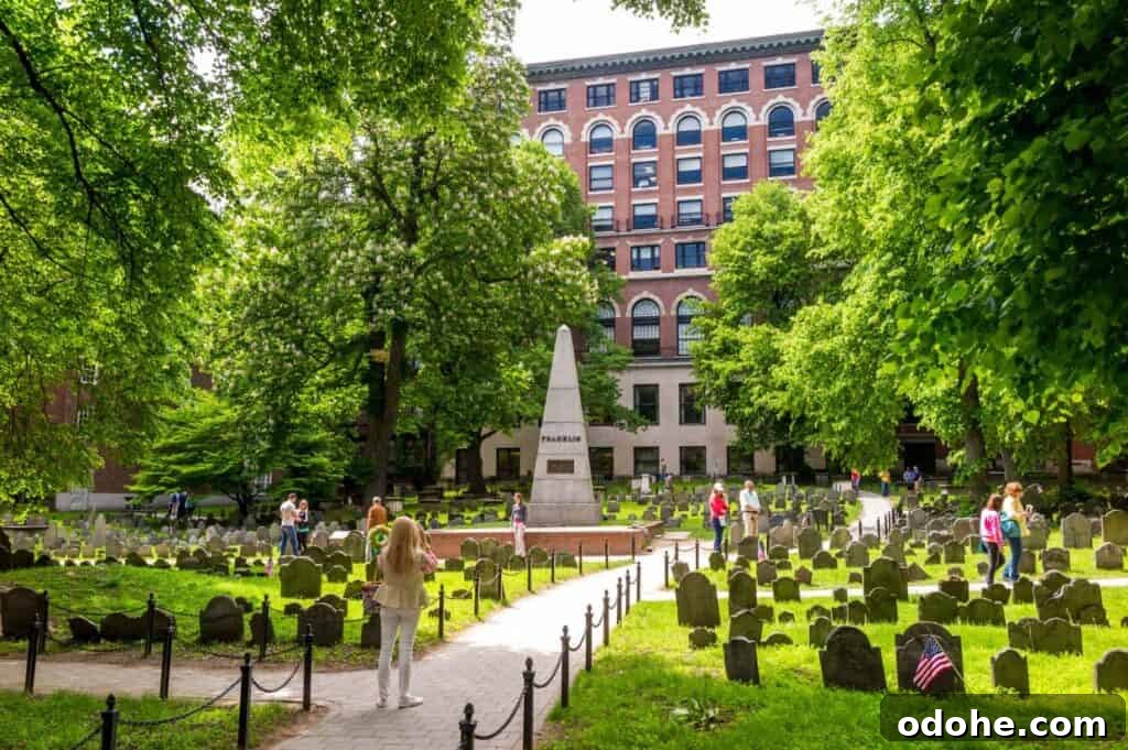 People enjoy walking tours in Boston's historic cemetery, where a central obelisk is surrounded by tombstones and lush trees. A charming brick building stands in the background, adding to the scene's timeless beauty.