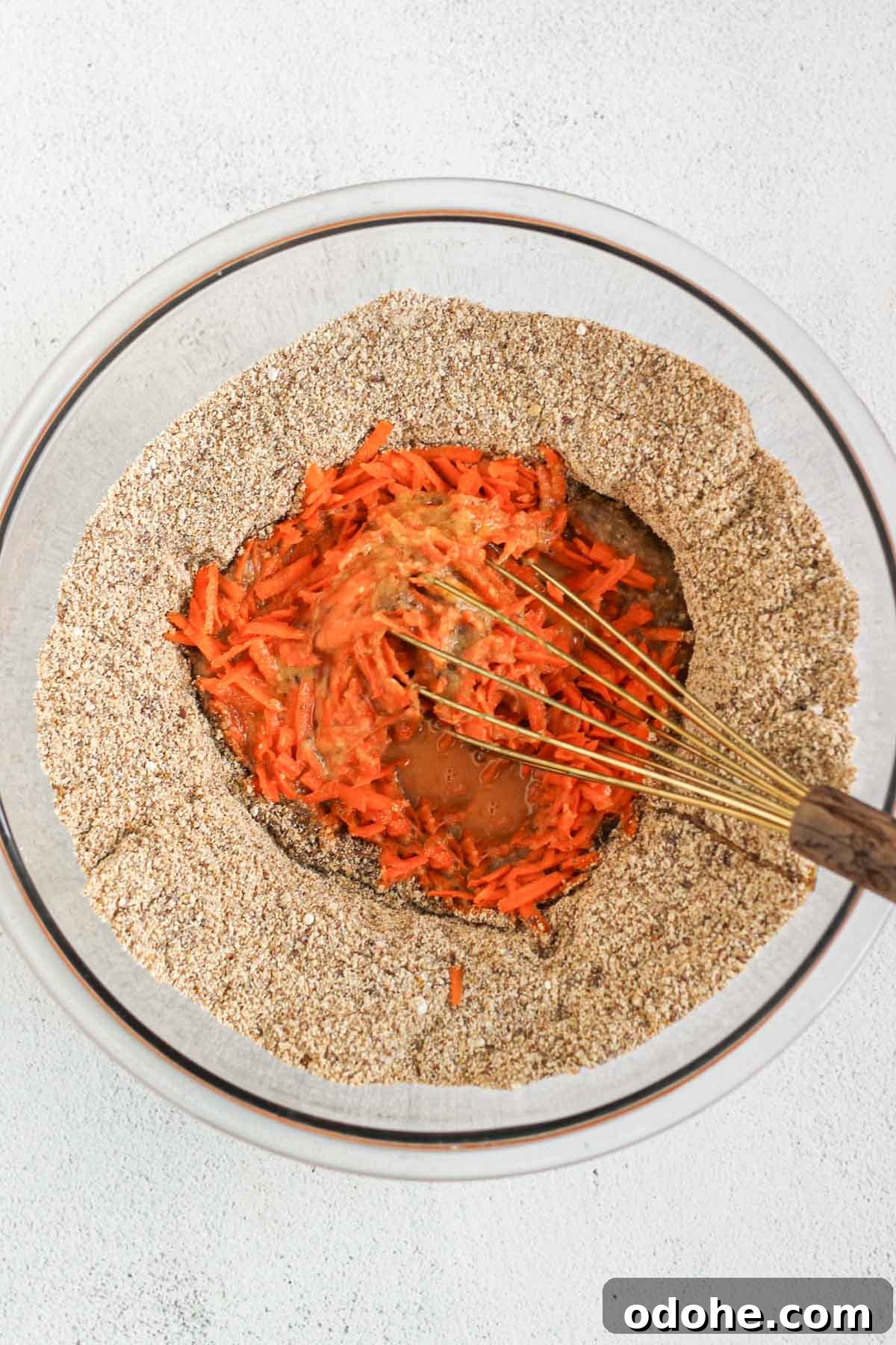 Flaxseed Carrot Muffins with Cinnamon and Honey 5 Glass mixing bowl with dry ingredients for carrot flaxseed muffins with wet ingredients in the center being mixed with a wire whisk.