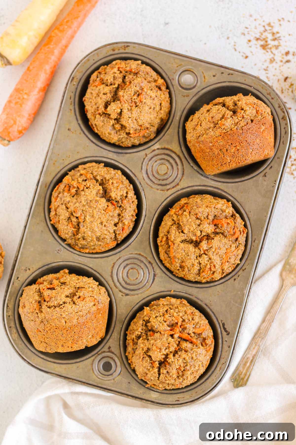 Flaxseed Carrot Muffins with Cinnamon and Honey 9 Carrot flaxseed muffins in a 6-cup vintage muffin tin with carrots on the side.