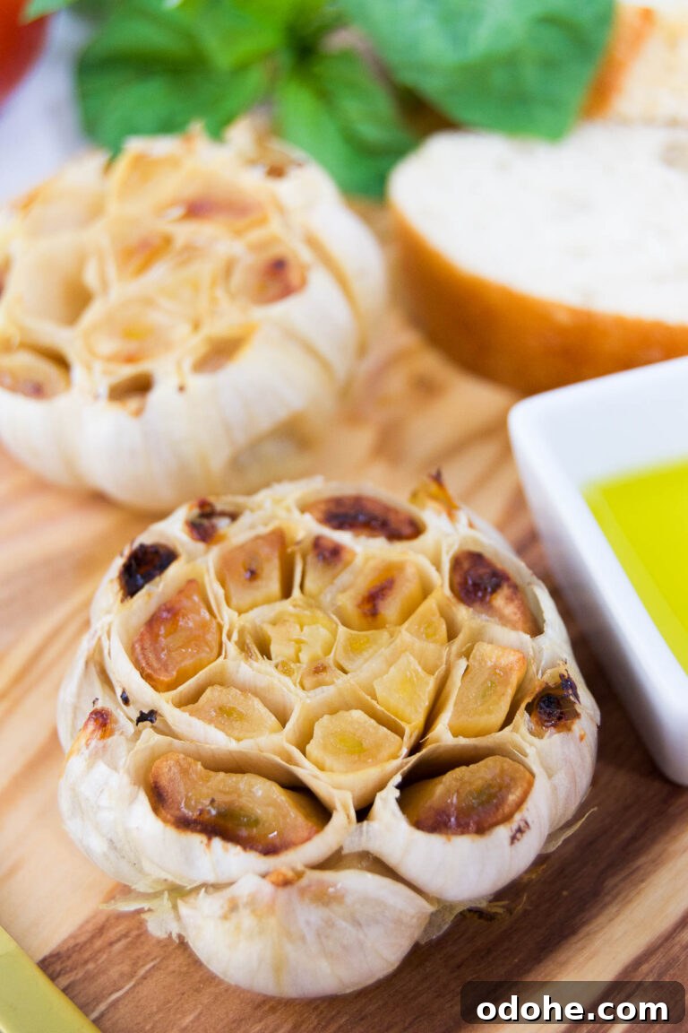 Air fryer roasted garlic cloves on a wooden cutting board next to olive oil and bread