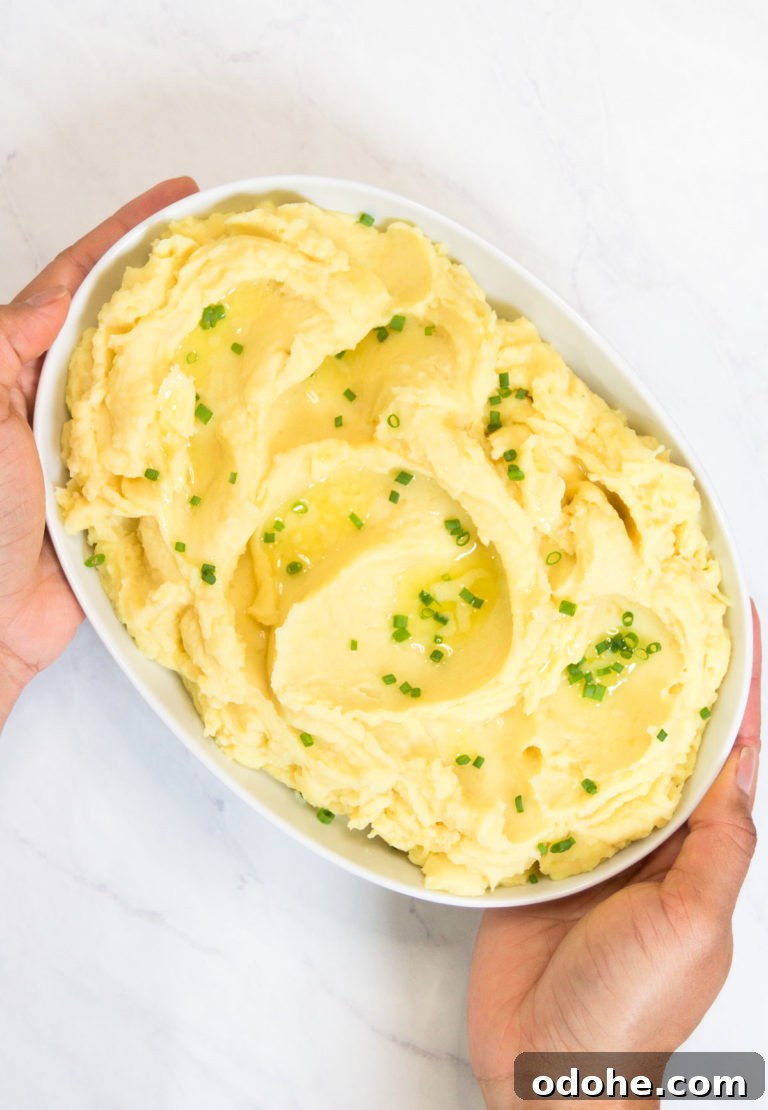 A woman holds a bowl of Instant Pot Mashed Potatoes garnished with butter and chives
