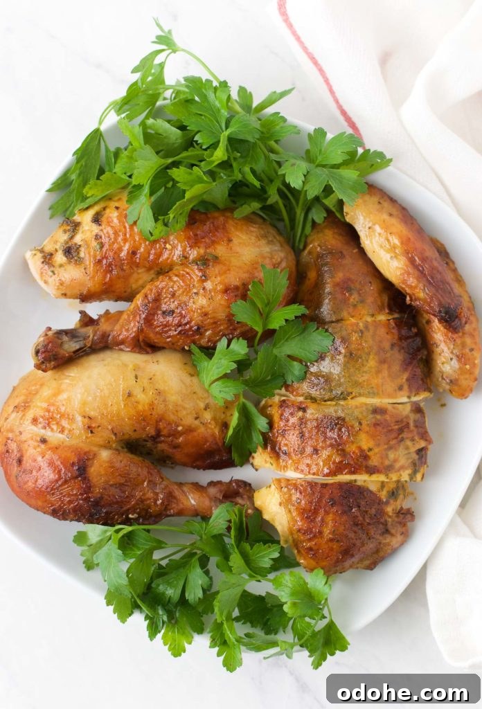 Sliced pieces of Oven Roasted Chicken sit on top of greens on a white plate
