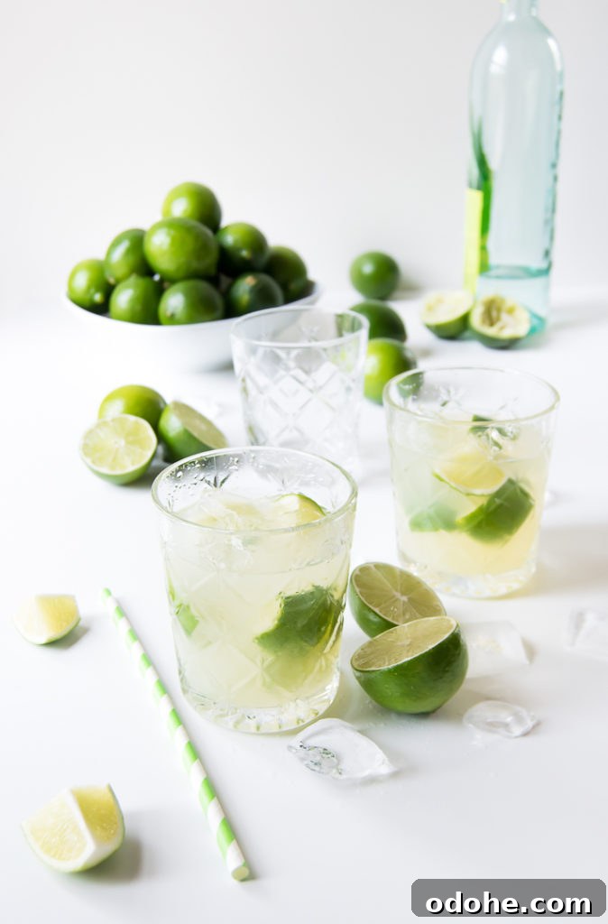 two caipirinhas on a white surface surrounded by ice and limes