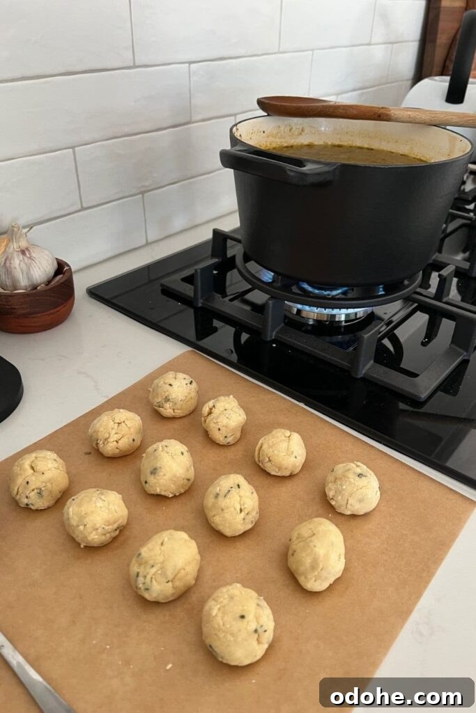 Sourdough Dumplings: Quick Discard and Overnight Methods 5 12 sourdough dumplings sitting on a piece of parchment paper. The dumplings are next to a black glass cooktop. There is a large black cast iron pot on the stove with simmering soup.