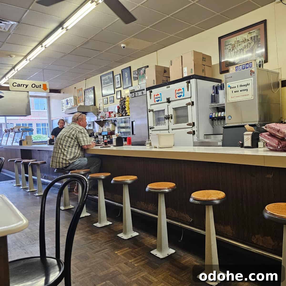 counter seating in Coney Island Hot Dog Fort Wayne with a pepsi sign, guy sitting at the counter, and carry out sign hanging from the ceiling