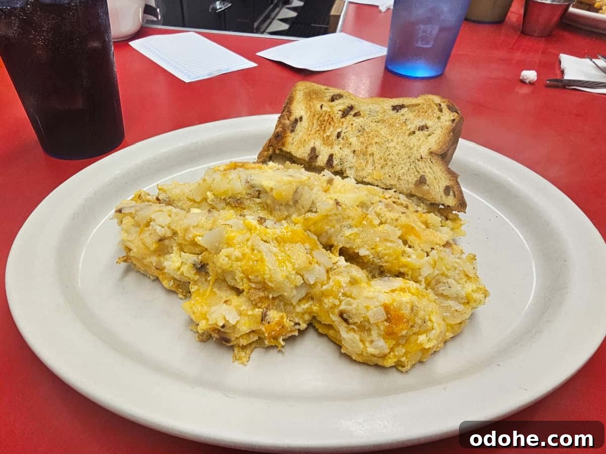 White plate with egg and hashbrown mix and raisin toast next to a diet coke