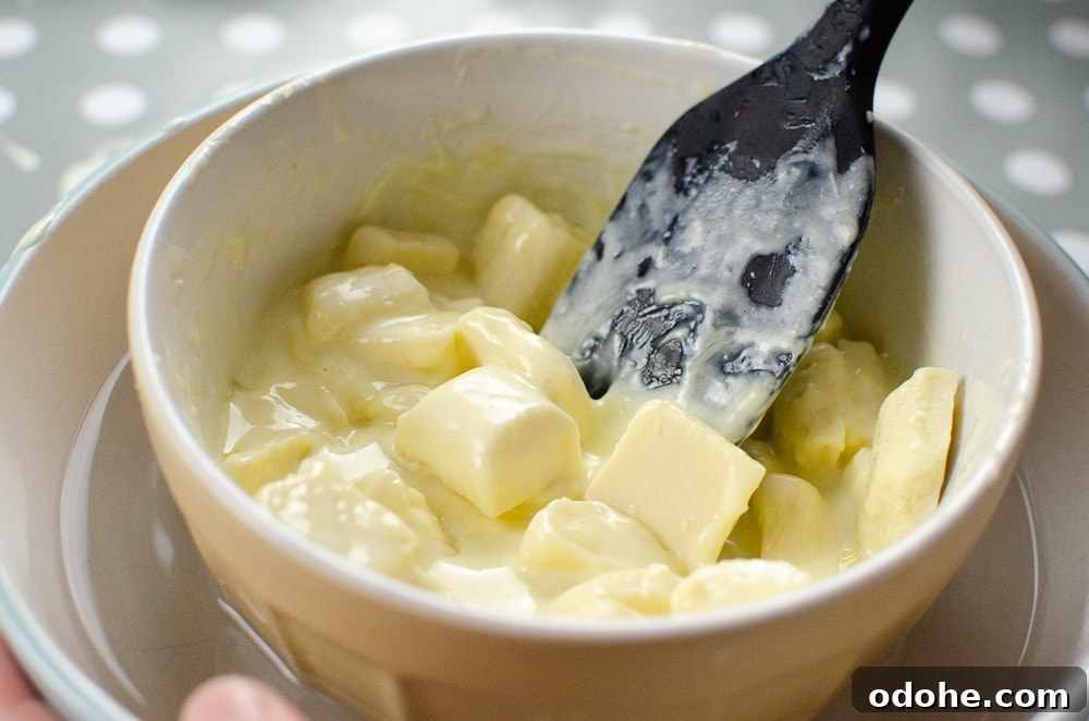 Decadent White Chocolate Truffles Recipe for Homemade Gifts 7 Mixing the cream and white chocolate together with a black spoon in a mixing bowl sitting in warm water