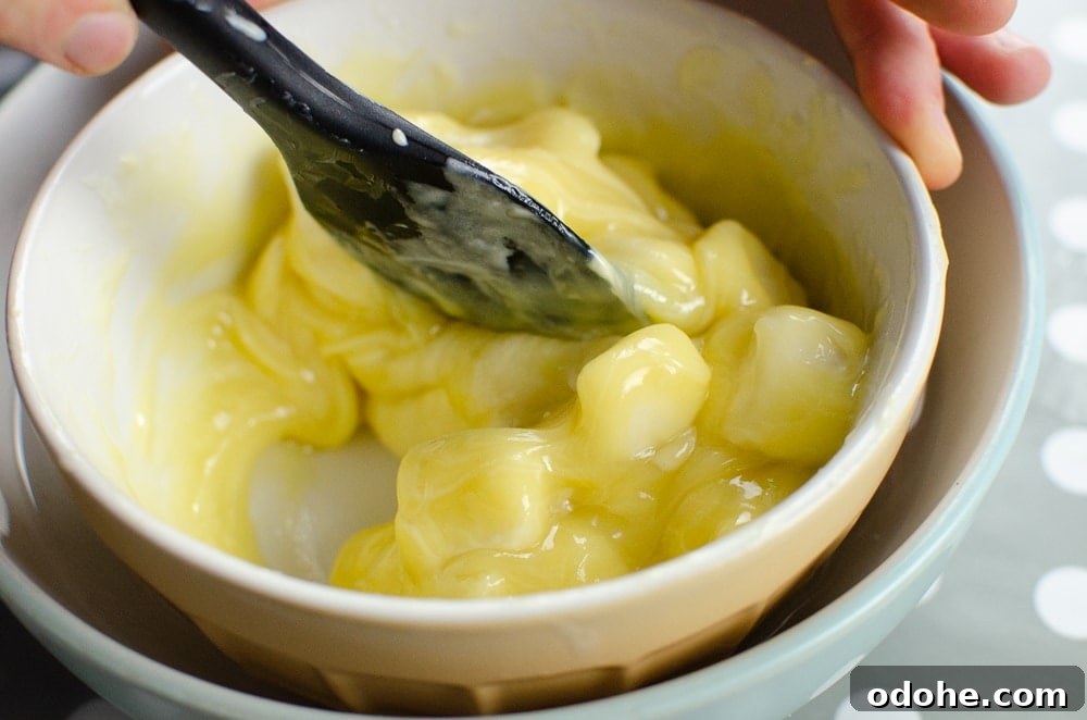 Decadent White Chocolate Truffles Recipe for Homemade Gifts 8 Mixing the cream and white chocolate together with a black spoon in a mixing bowl sitting in warm water to make our white chocolate truffles