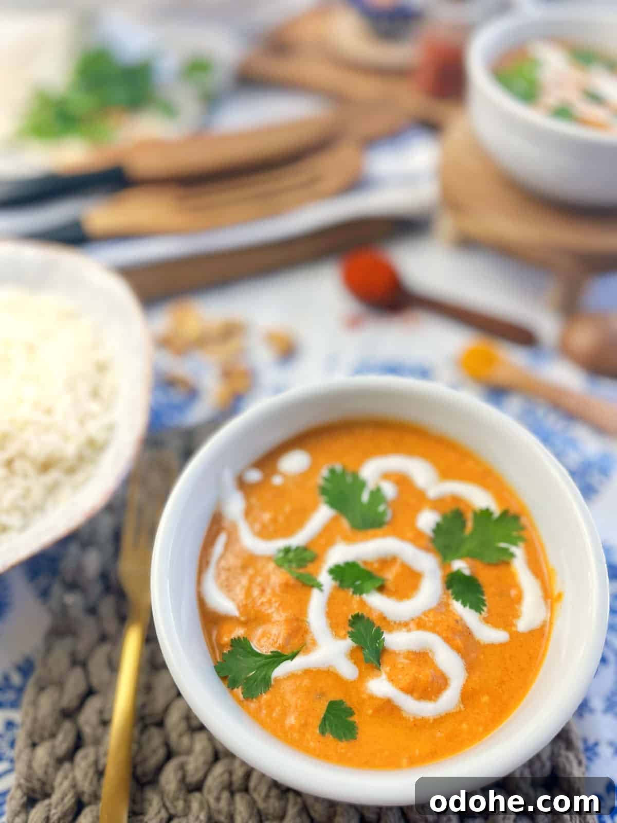 white bowl of red curry and bowl of rice with kitchen tools in background.