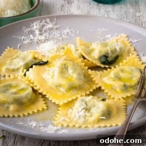 Fresh Spinach and Ricotta Ravioli Recipe for Homemade Pasta 18 Spinach Ricotta ravioli on a off white plate with a sprinkle of finely grated cheese.