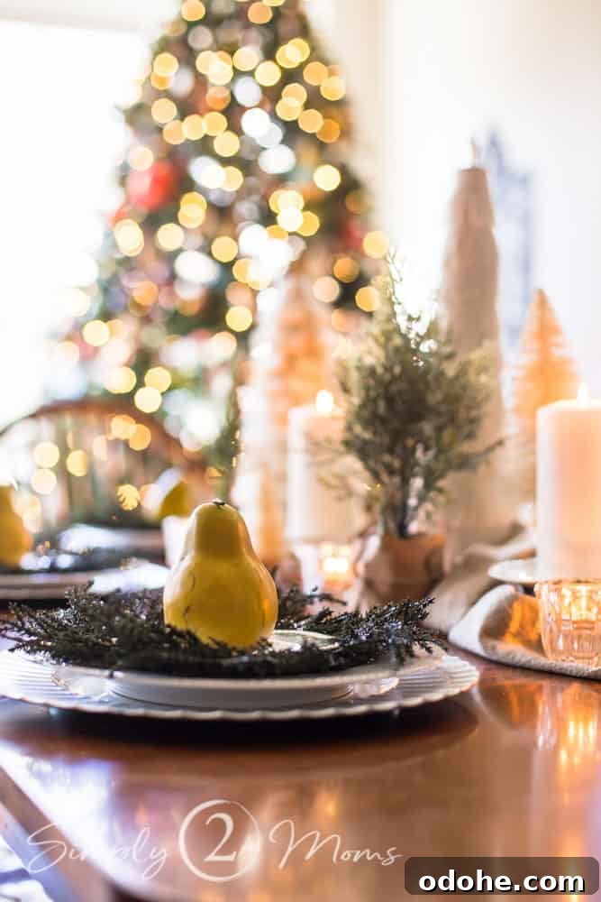 13 Timeless Neutral Christmas Decorating Ideas for Your Home 19 Side view of Simple Christmas table setting with a charger, plate, wreath, Wedgewood bread plate, topped with a yellow faux pear with greenery and white burlap trees centerpiece in the background