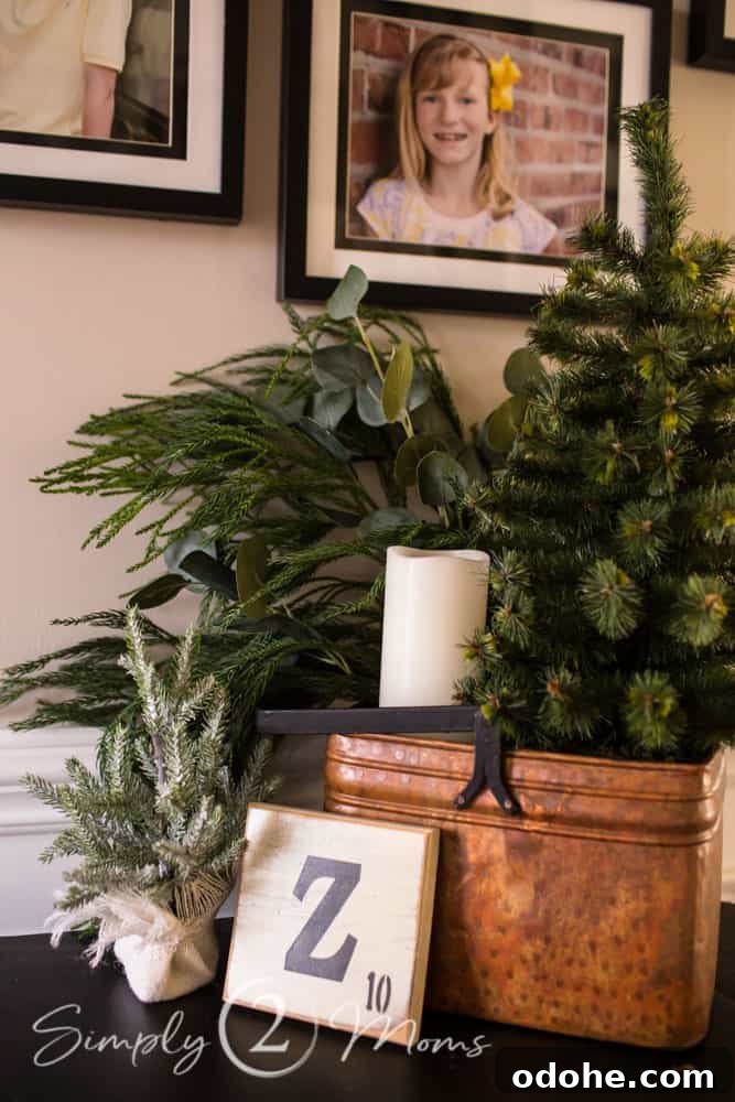 13 Timeless Neutral Christmas Decorating Ideas for Your Home 4 Rectangular antique copper bucket filled with Christmas greenery and a faux candle sitting on a table with a mini tree in front and a large Z scrabble square leaning against it.