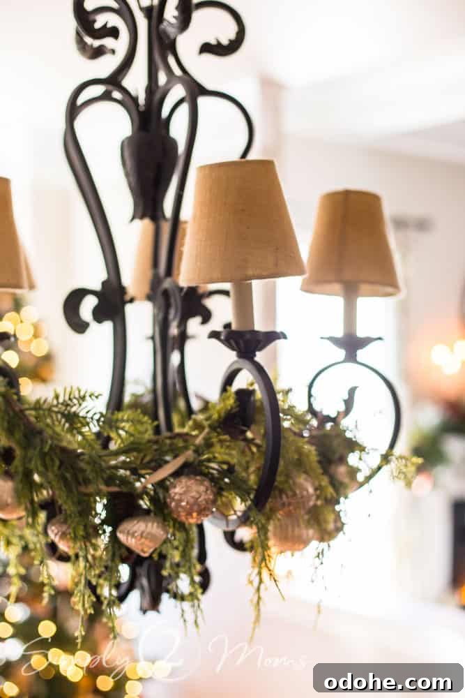13 Timeless Neutral Christmas Decorating Ideas for Your Home 6 Black iron French country chandelier with burlap candle shades decorated for Christmas with natural greenery and vintage ornament garland.