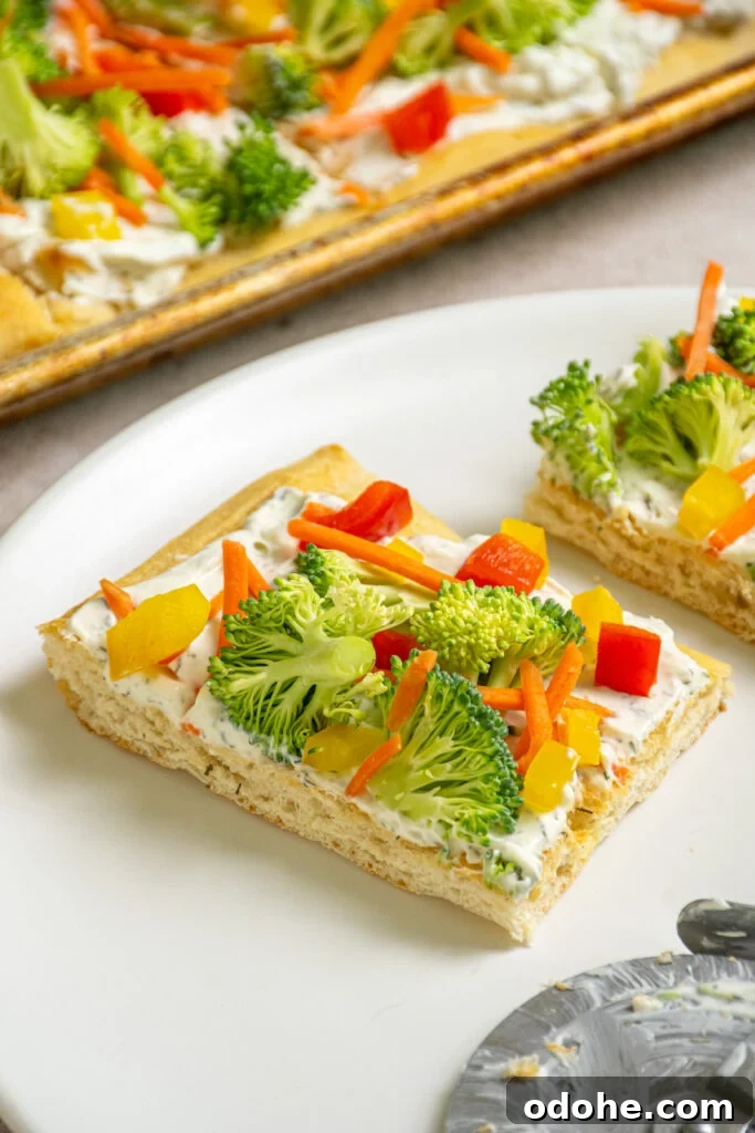 A slce of crescent roll veggie pizza on a white plate topped with fresh broccoli, carrots, and bell peppers. 