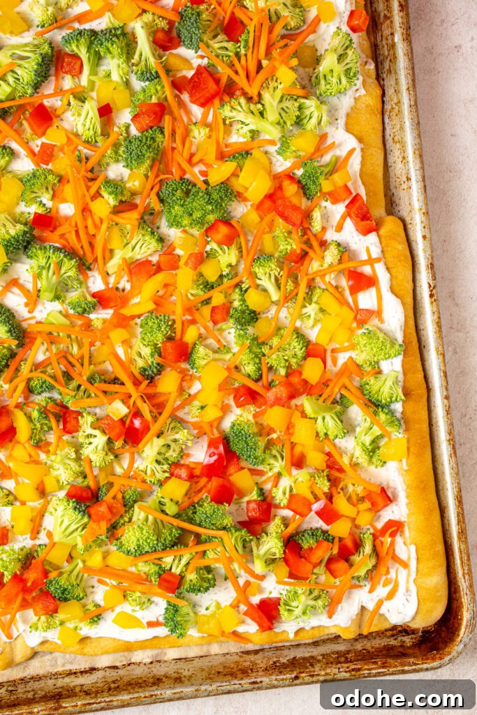 Crescent roll veggie pizza on a sheet pan piled high with broccoli, carrots, and bell peppers.